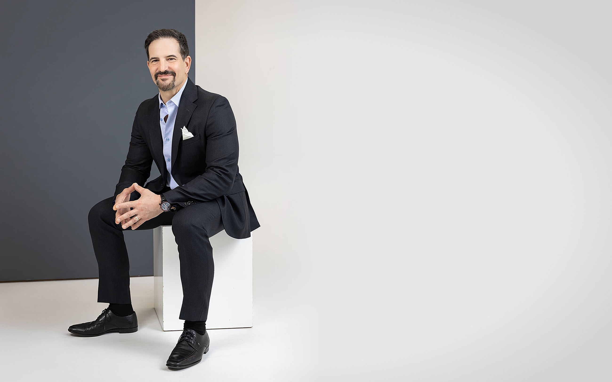 Man in suit sitting on a white cube.