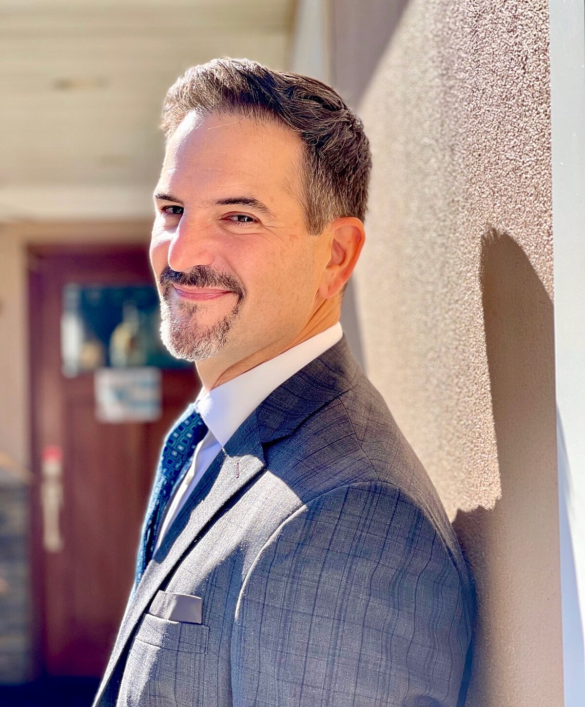 Man in suit smiling against a wall.