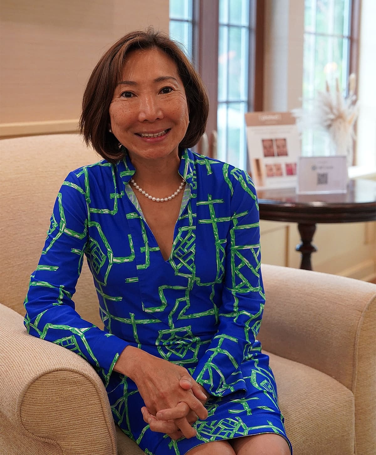 Smiling woman in blue patterned dress, relaxed setting.