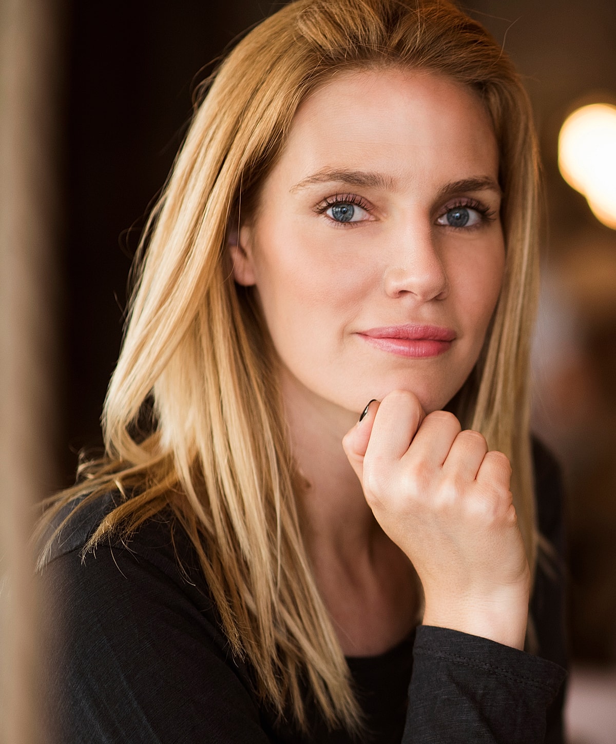 Woman smiling with hand on chin, soft background.