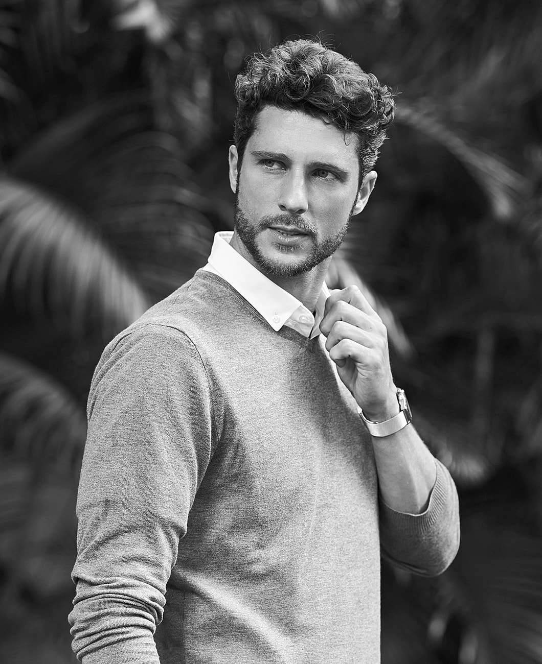 Man in gray sweater adjusting collar outdoors