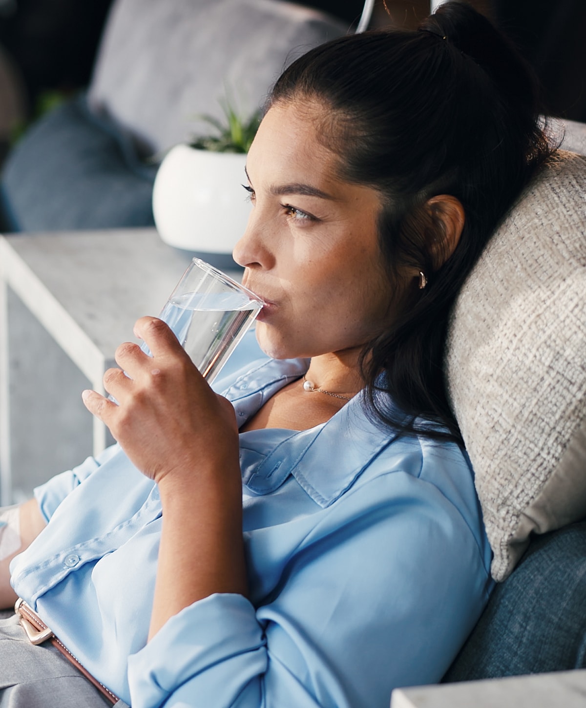 Woman sipping water, relaxing on a sofa.