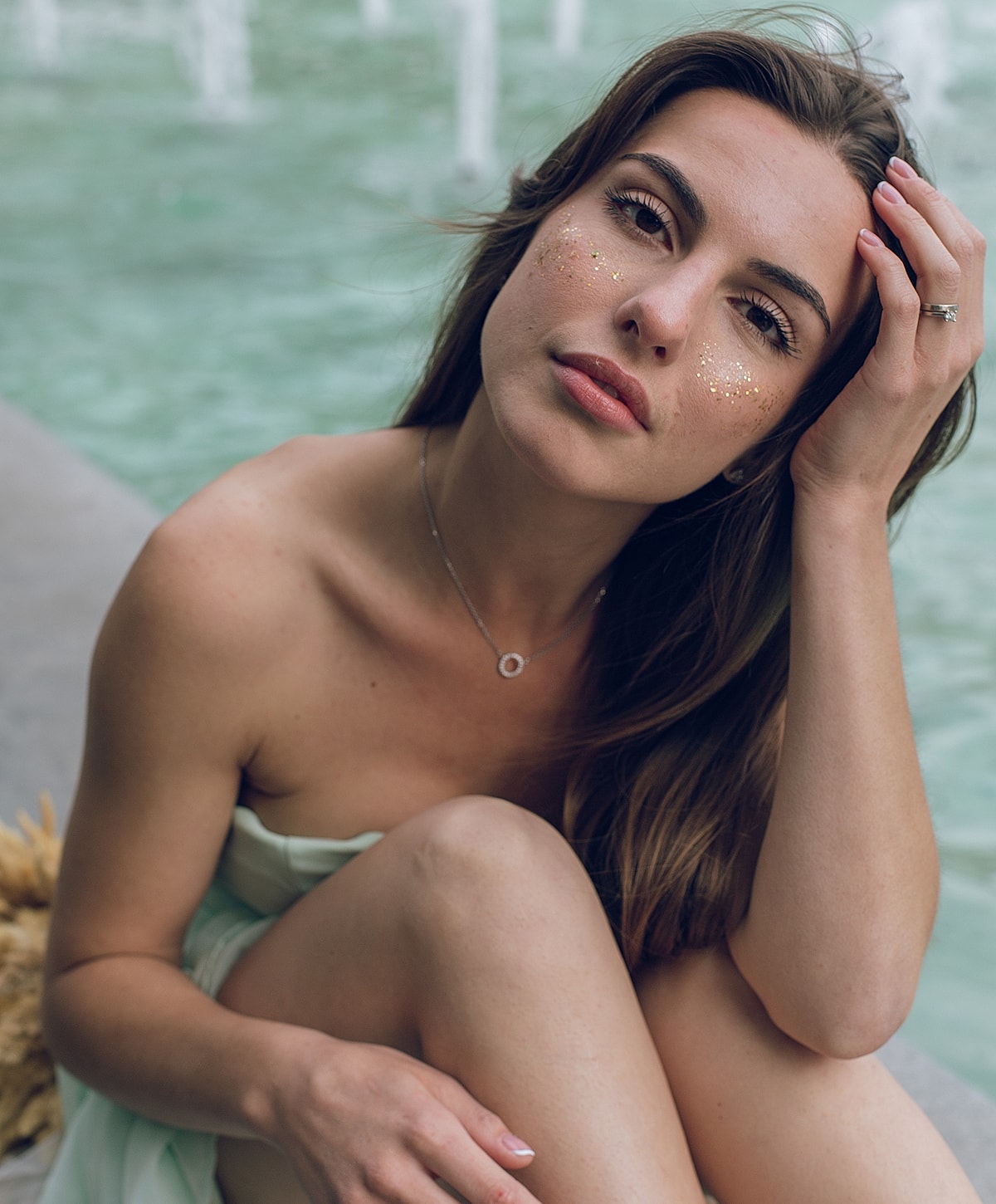 Woman sitting by water with glitter makeup.