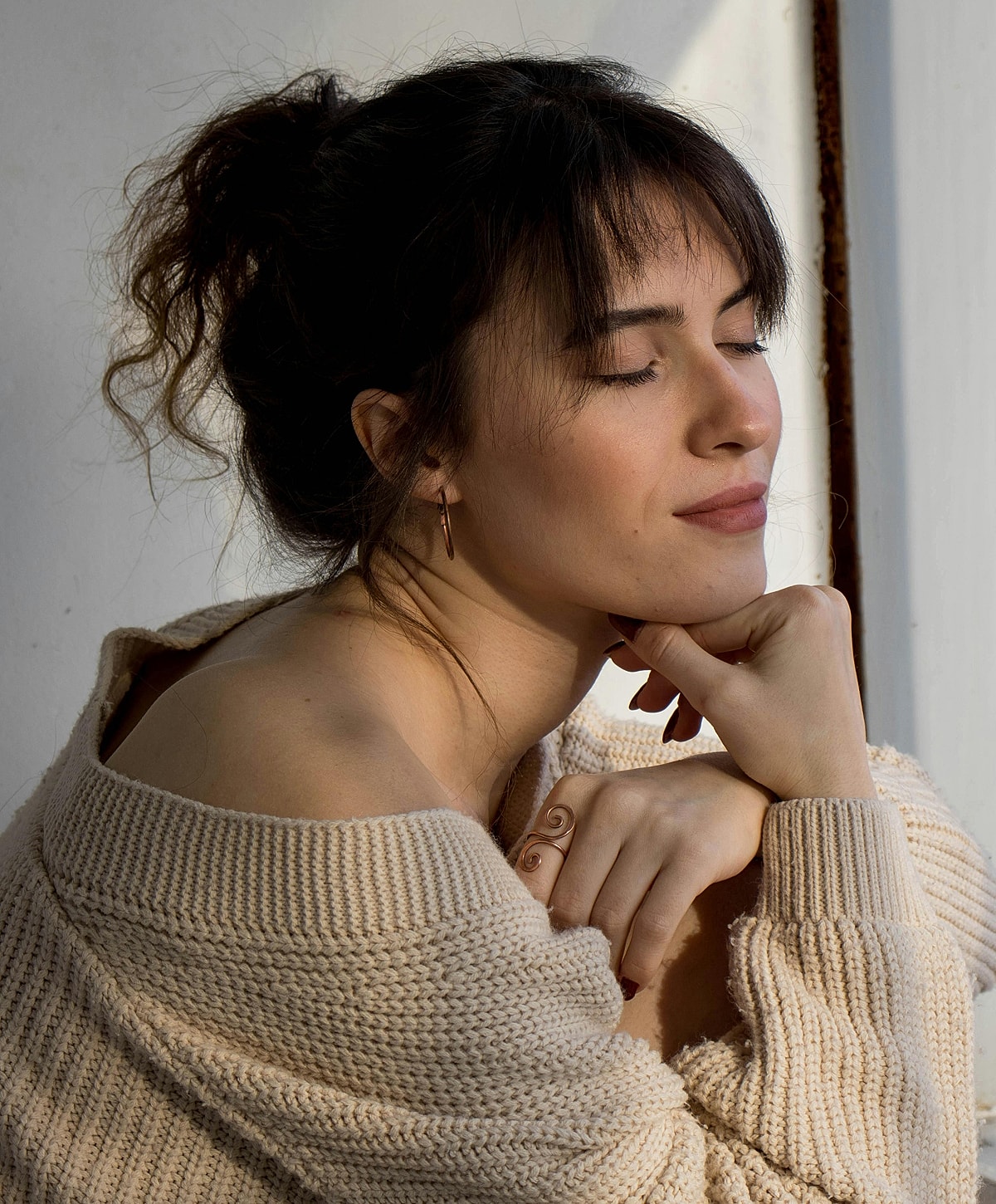 Woman in soft light, serene expression, cozy sweater.