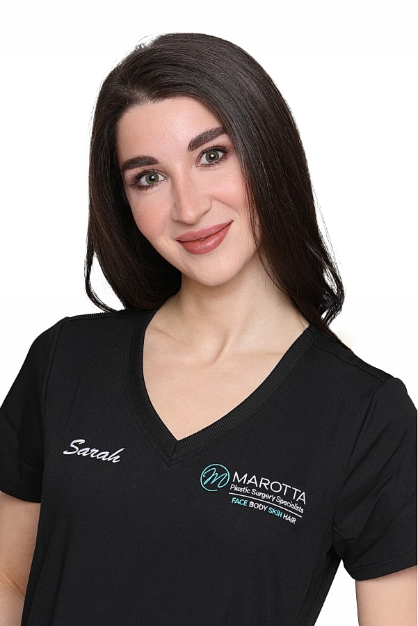 Smiling woman in medical scrubs with logo.