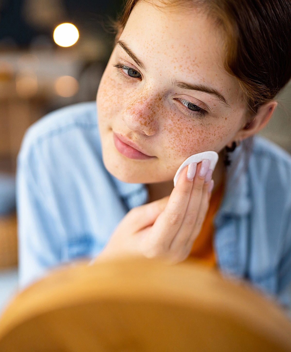 Girl applying skincare product in front of mirror.
