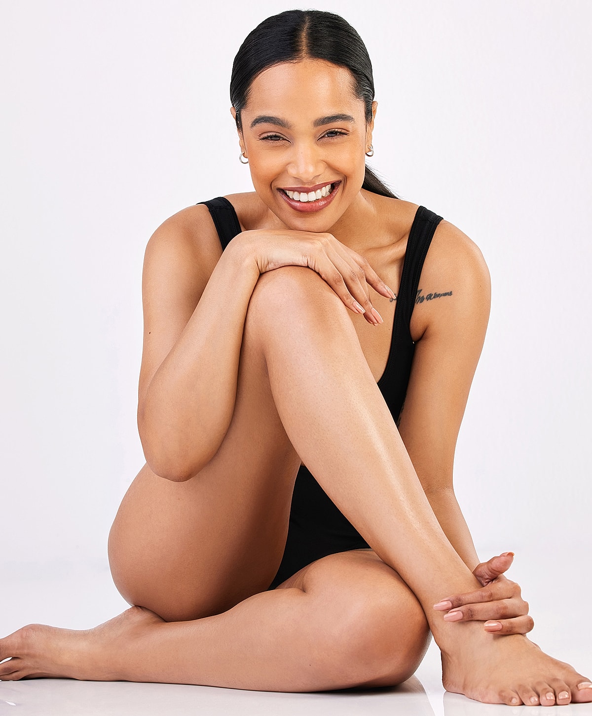 Smiling woman in black swimsuit, sitting pose.
