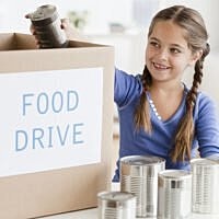 Girl donating to food drive with canned goods.