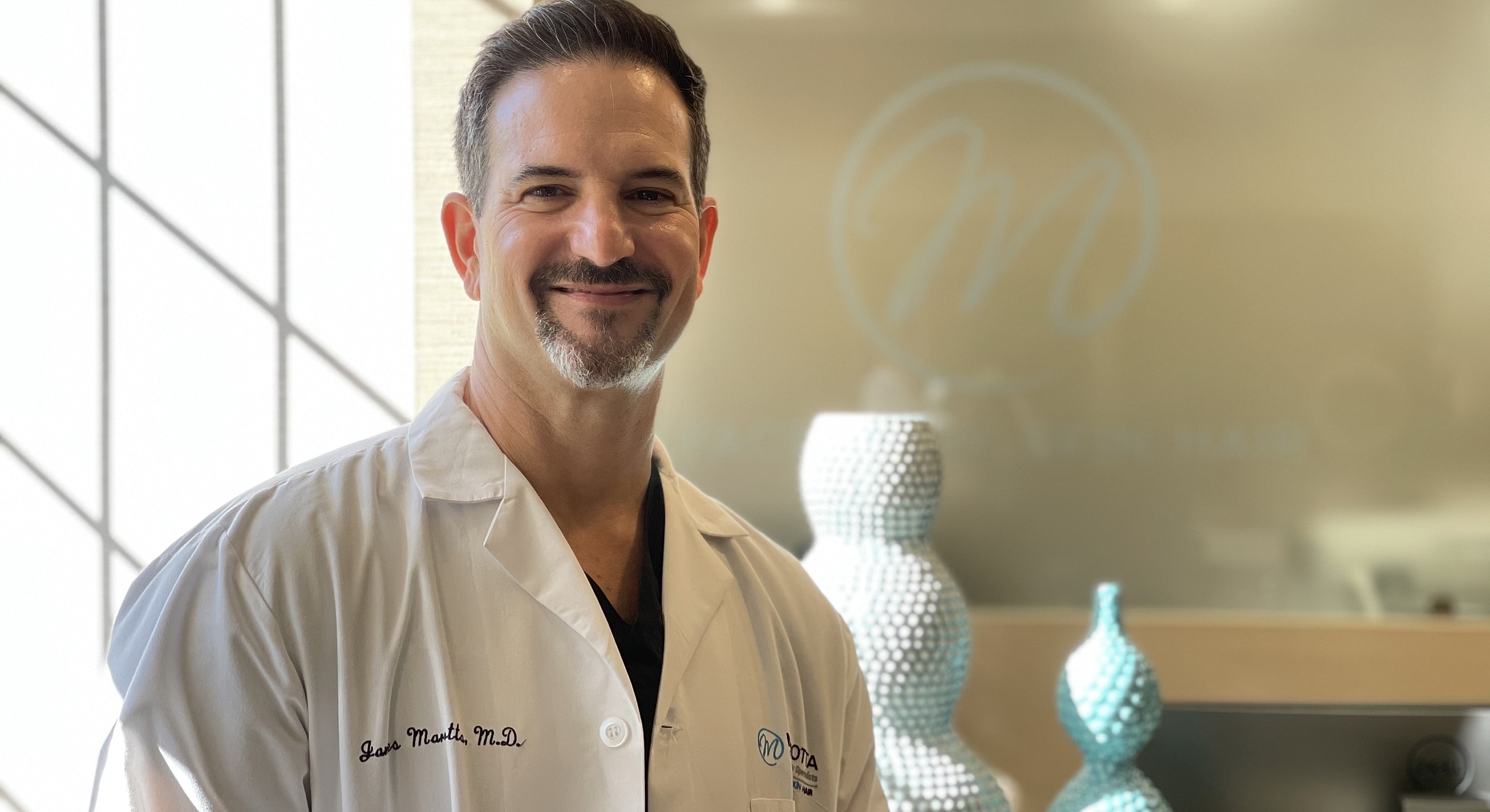 Doctor in a white coat, smiling at office.