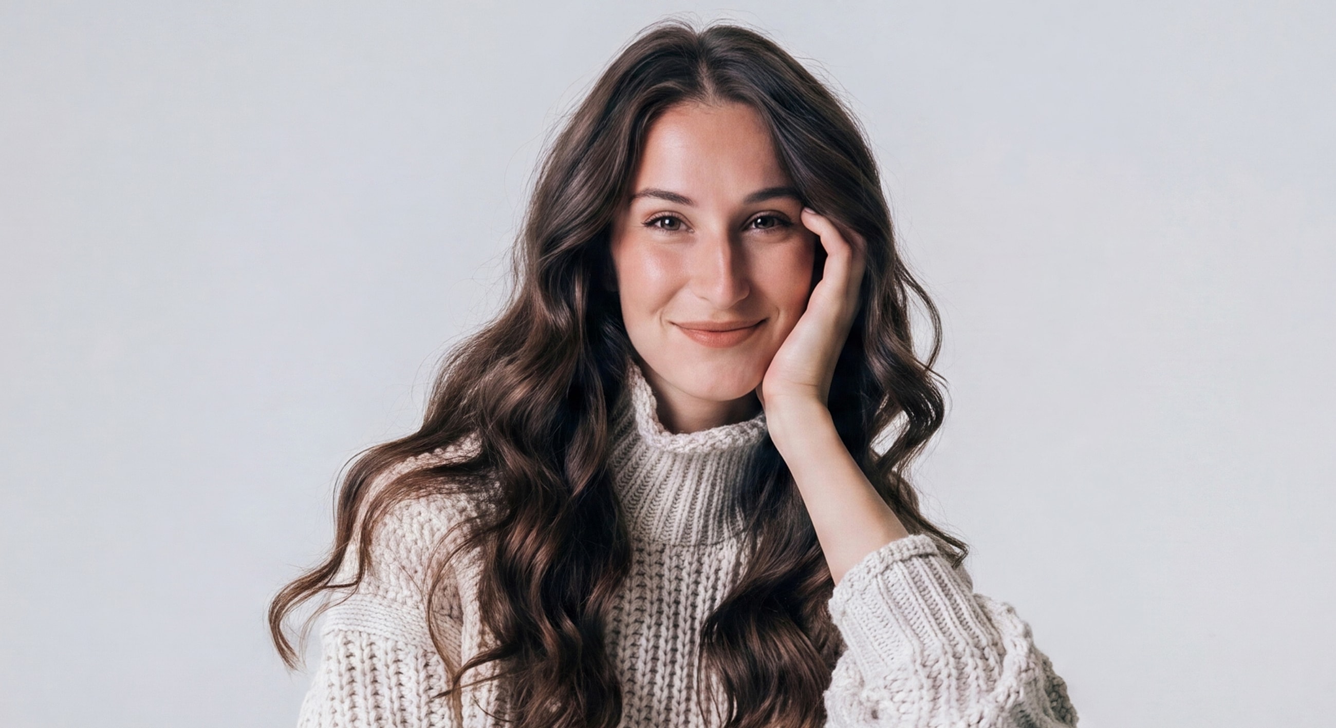 Smiling woman in cozy sweater against neutral background.