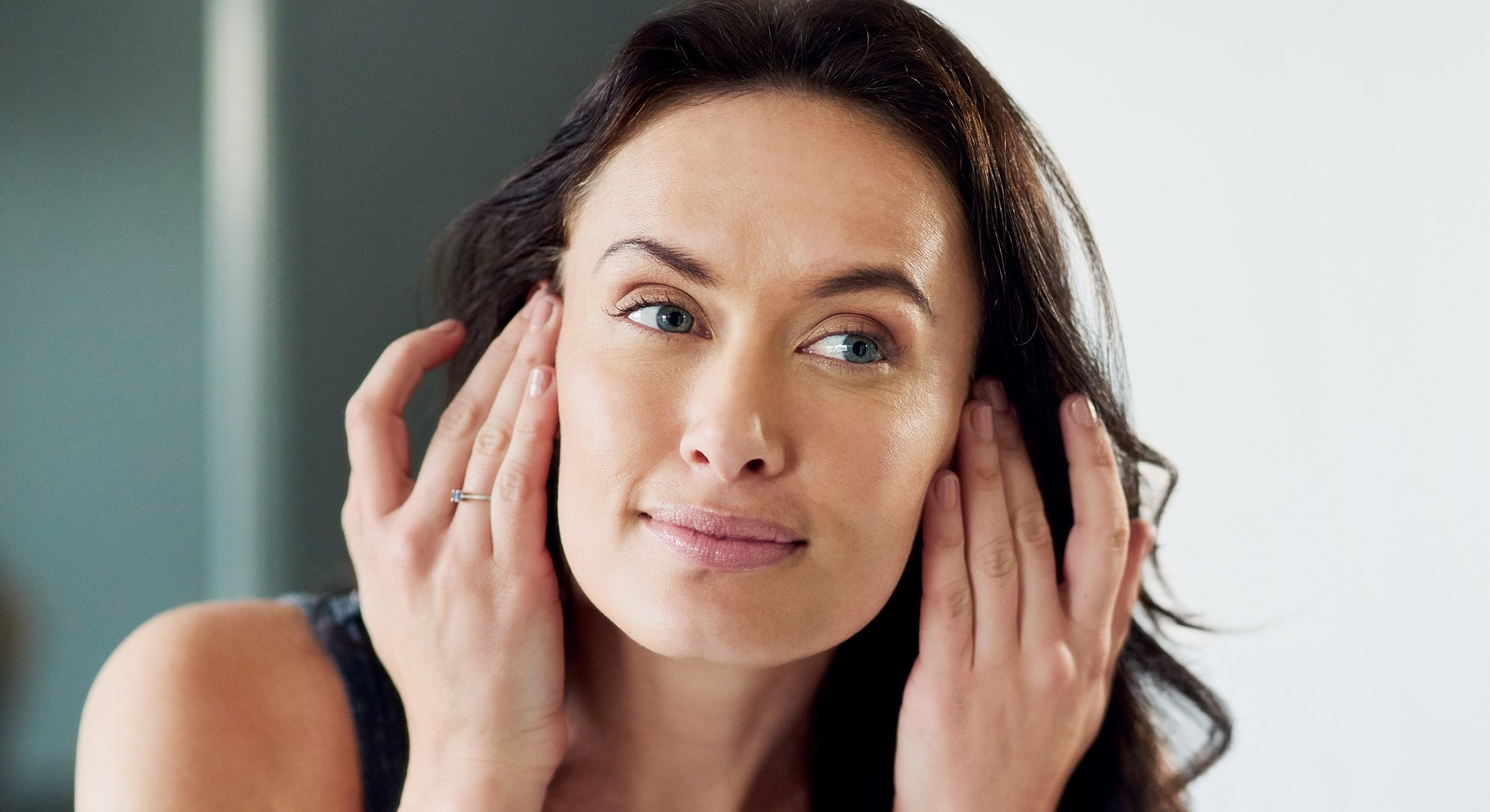 Woman applying skincare while looking in mirror