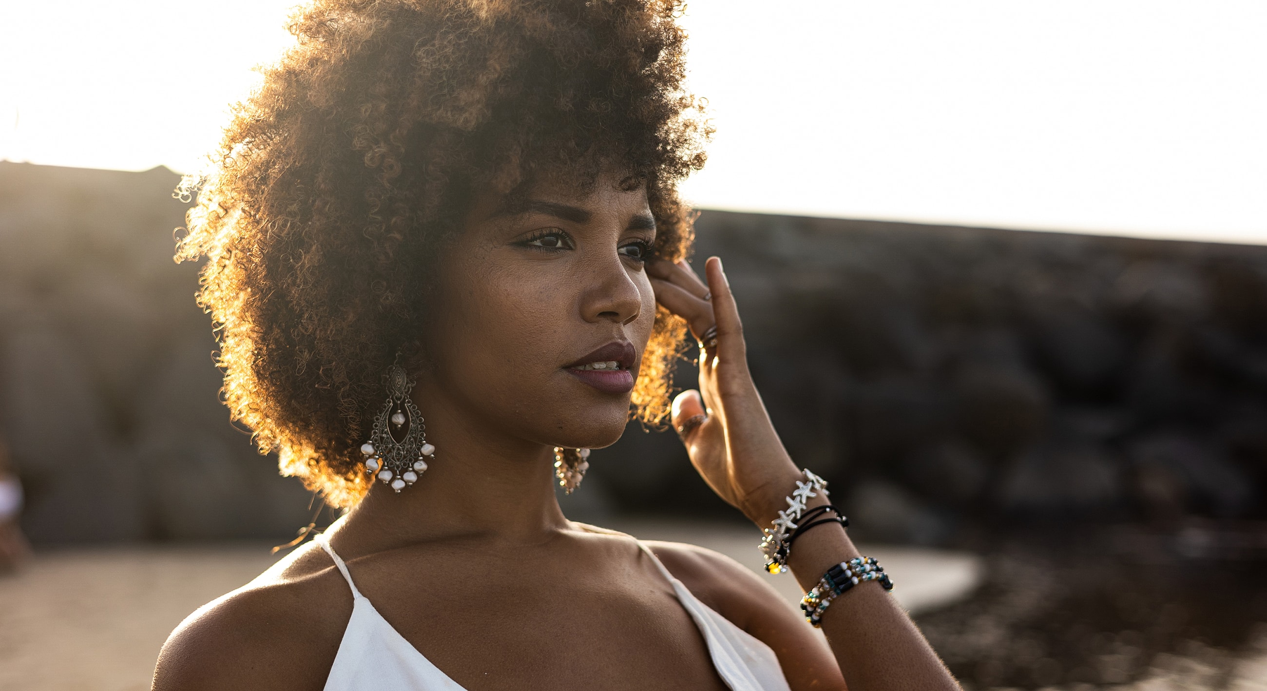 Woman with curly hair by the beach at sunset.