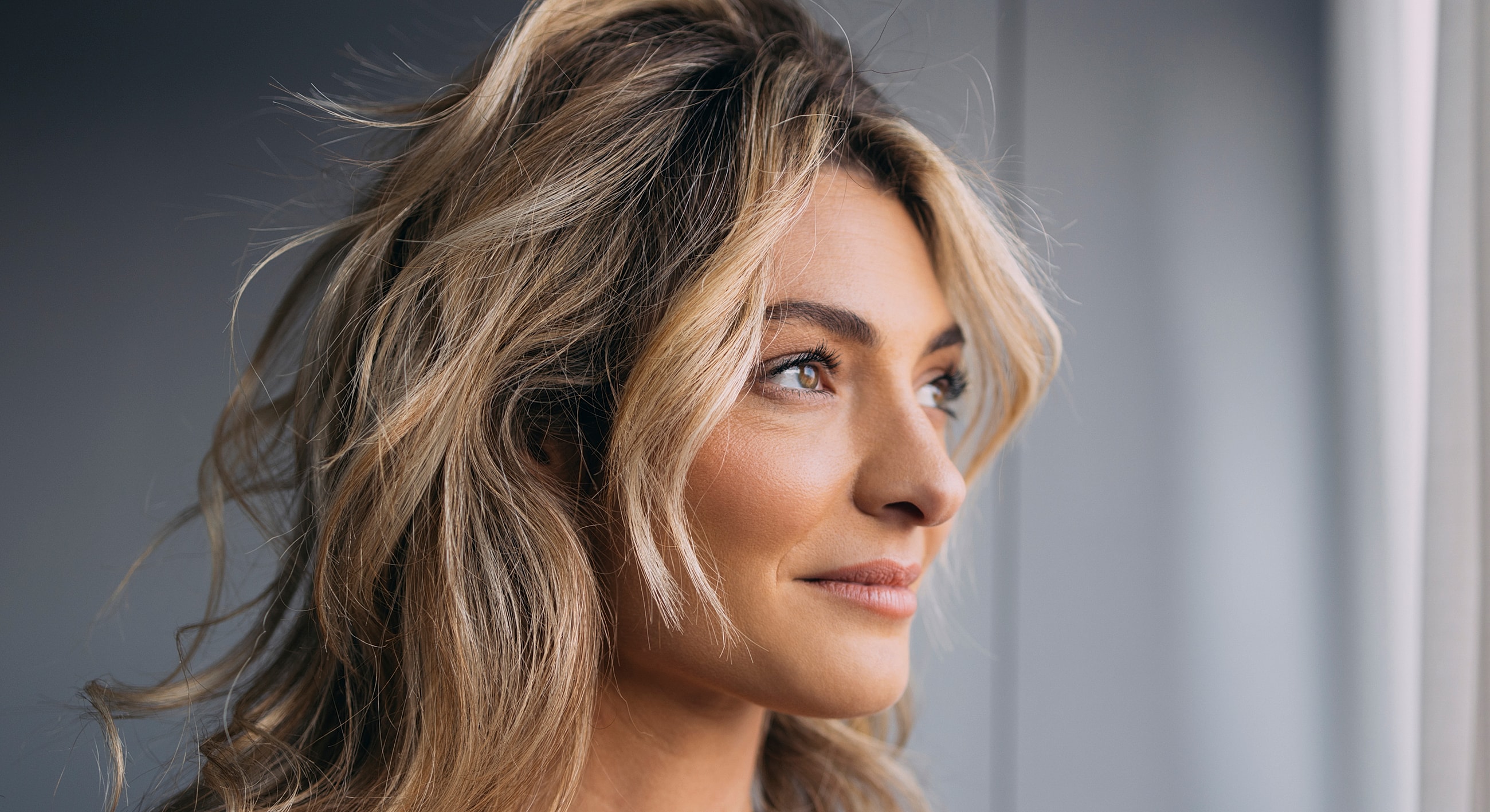 Woman with wavy hair looking out a window.