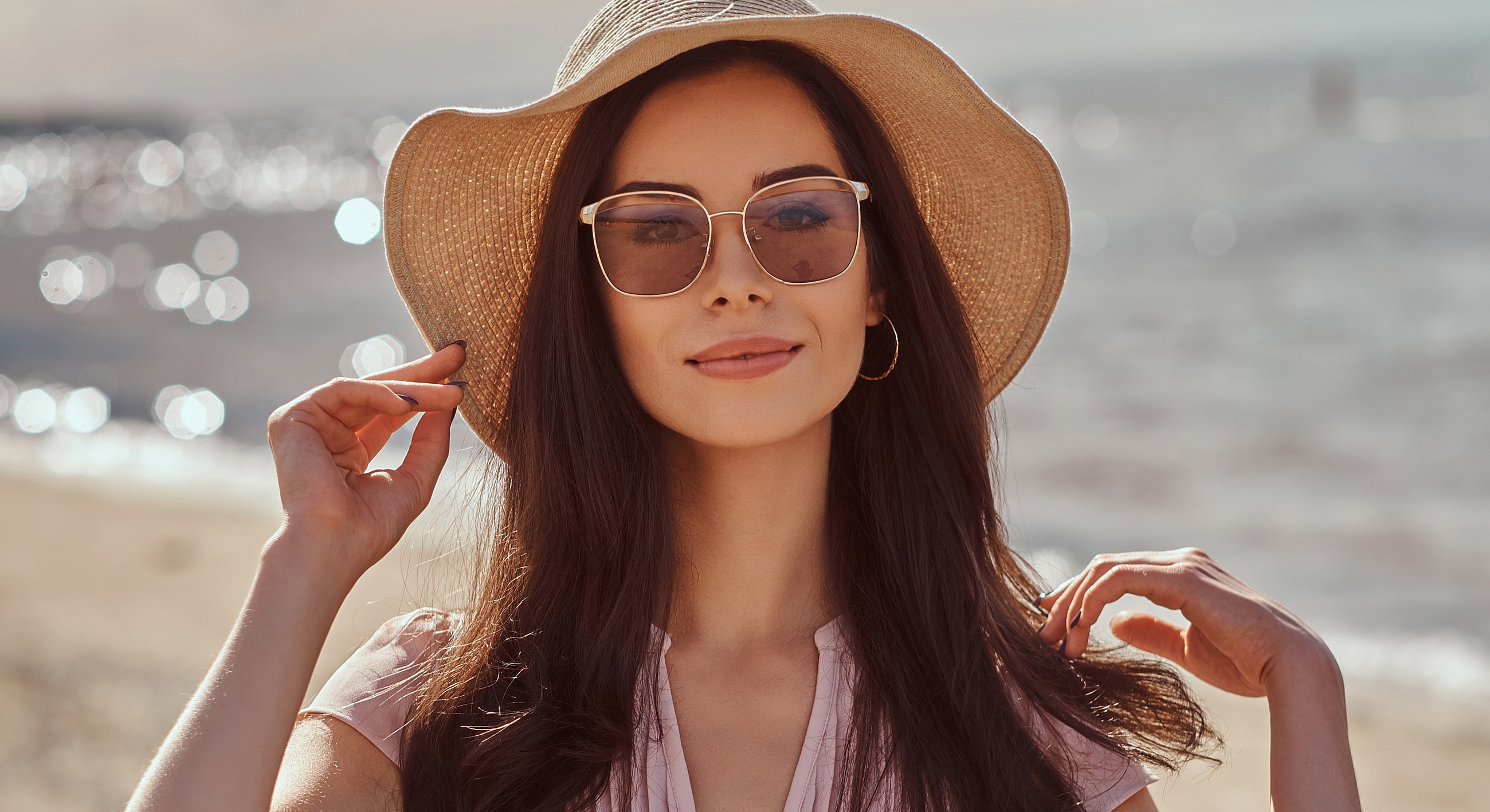 Woman in sunglasses and hat by the beach.
