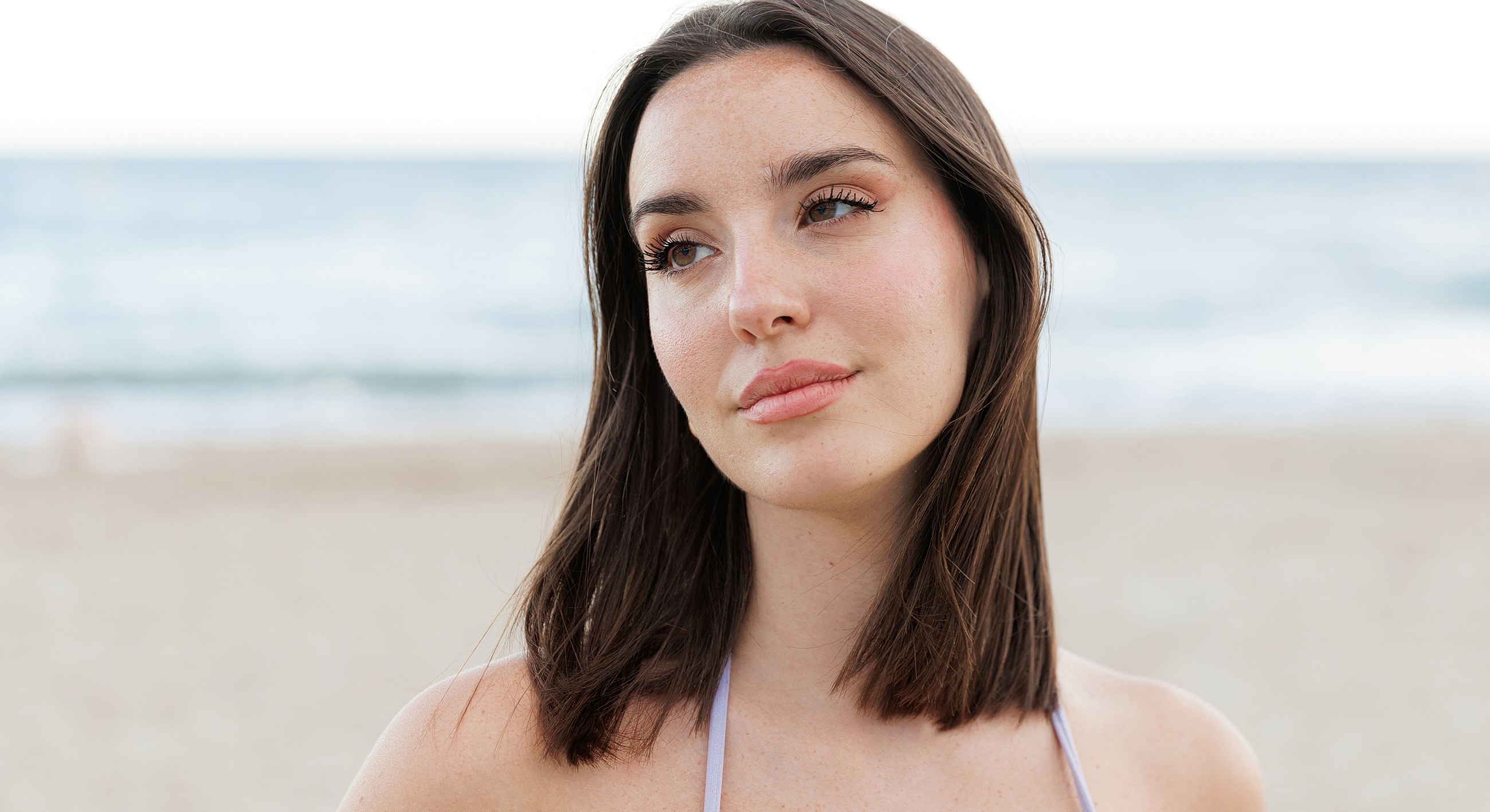 Young woman at the beach, thoughtful expression.