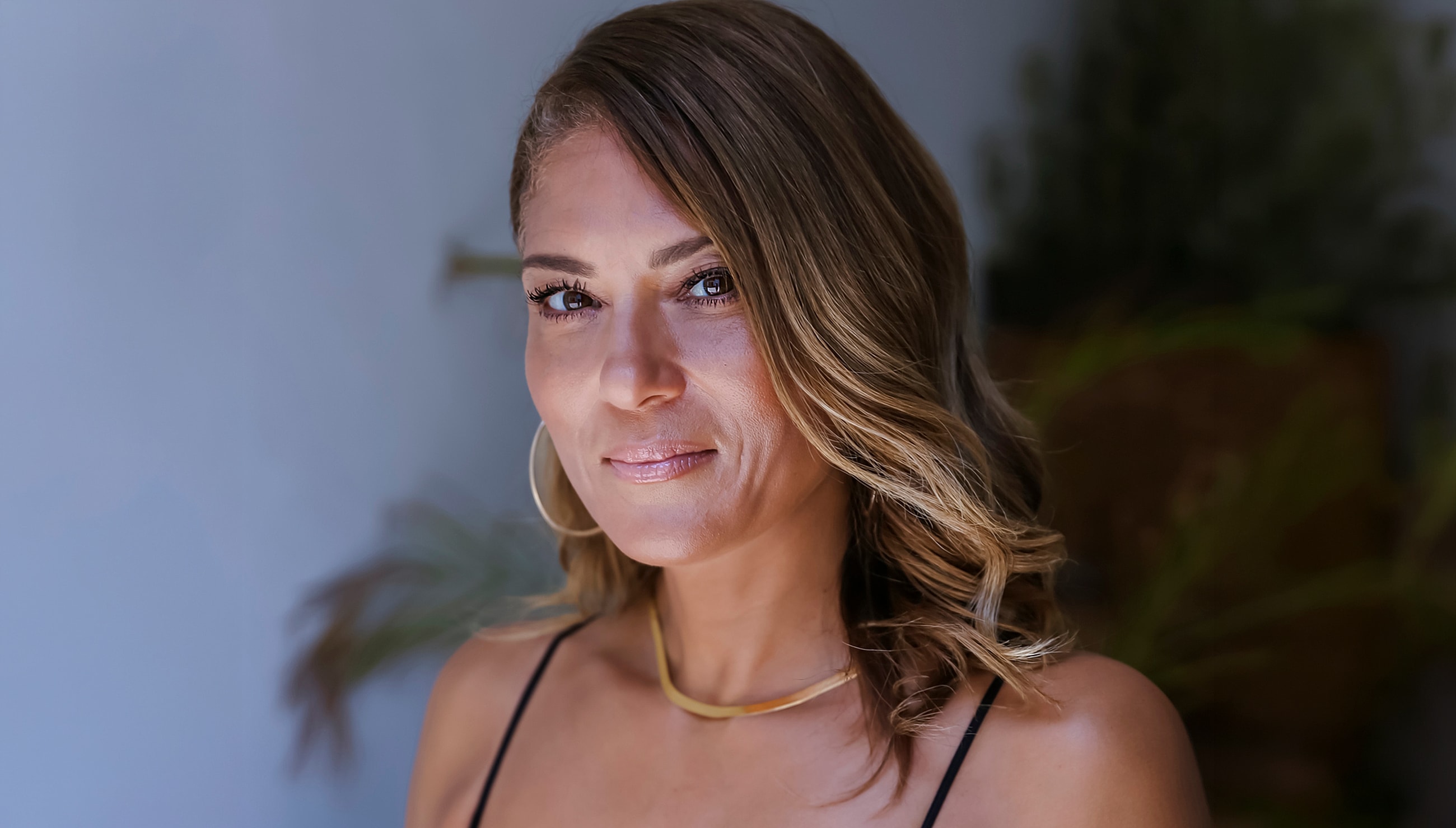 Smiling woman with wavy hair and gold jewelry.