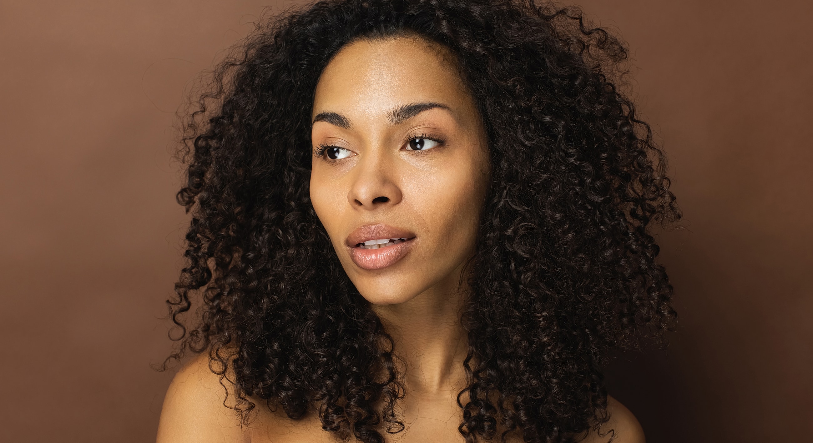 Woman with curly hair against brown background.